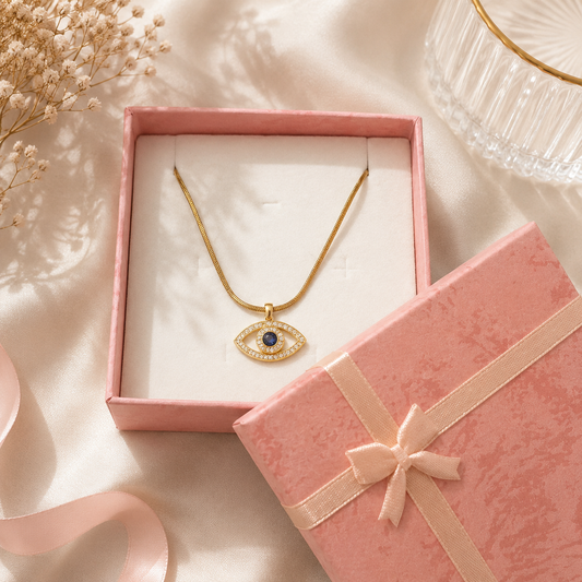Gold necklace with an eye-shaped pendant in a pink jewelry box on a soft beige background.