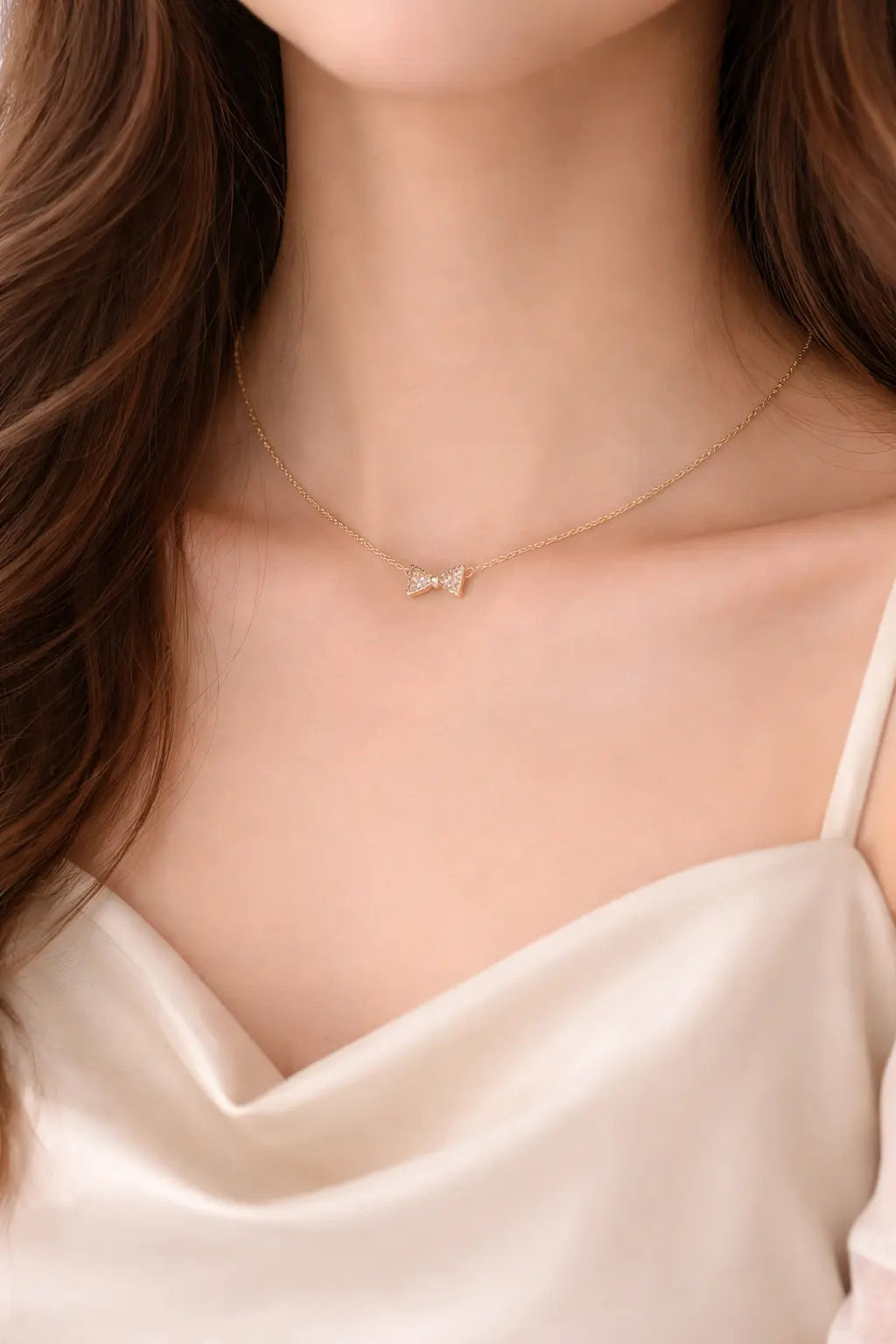 Gold necklace with a small pendant worn by a person in a satin top