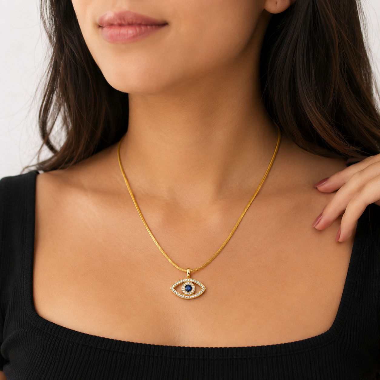 Woman wearing a gold necklace with an eye-shaped pendant on a plain background