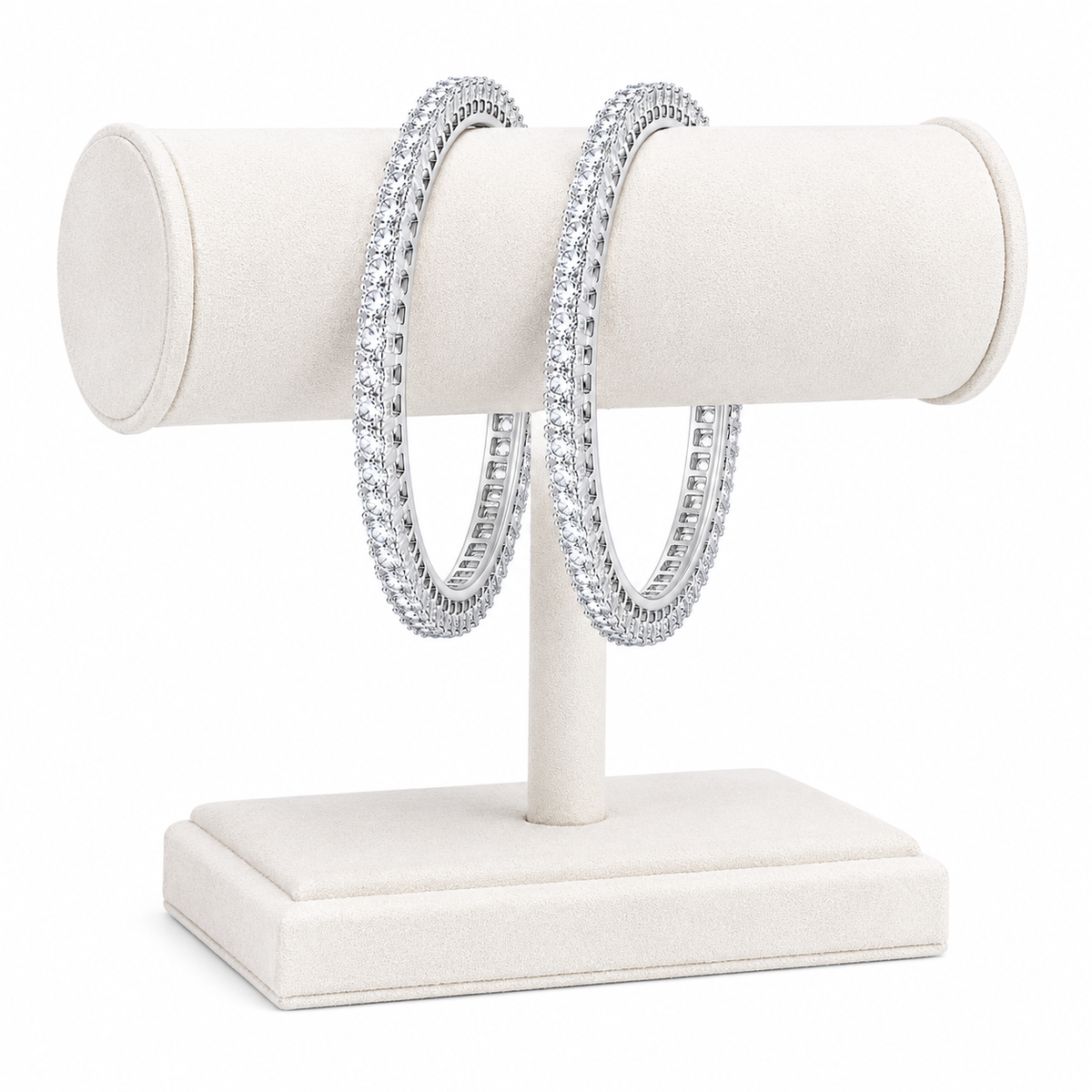 A pair of silver-toned hoop earrings covered in clear pavé stones, displayed on a cream-colored jewelry stand against a white background.