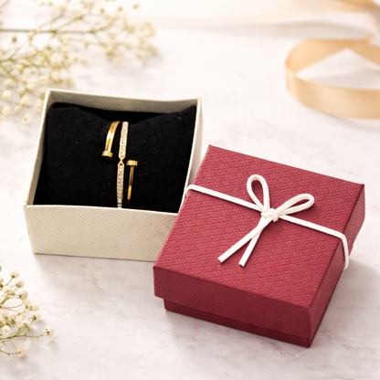 Gold earrings in an open jewelry box with a red box featuring a white bow on a light background.