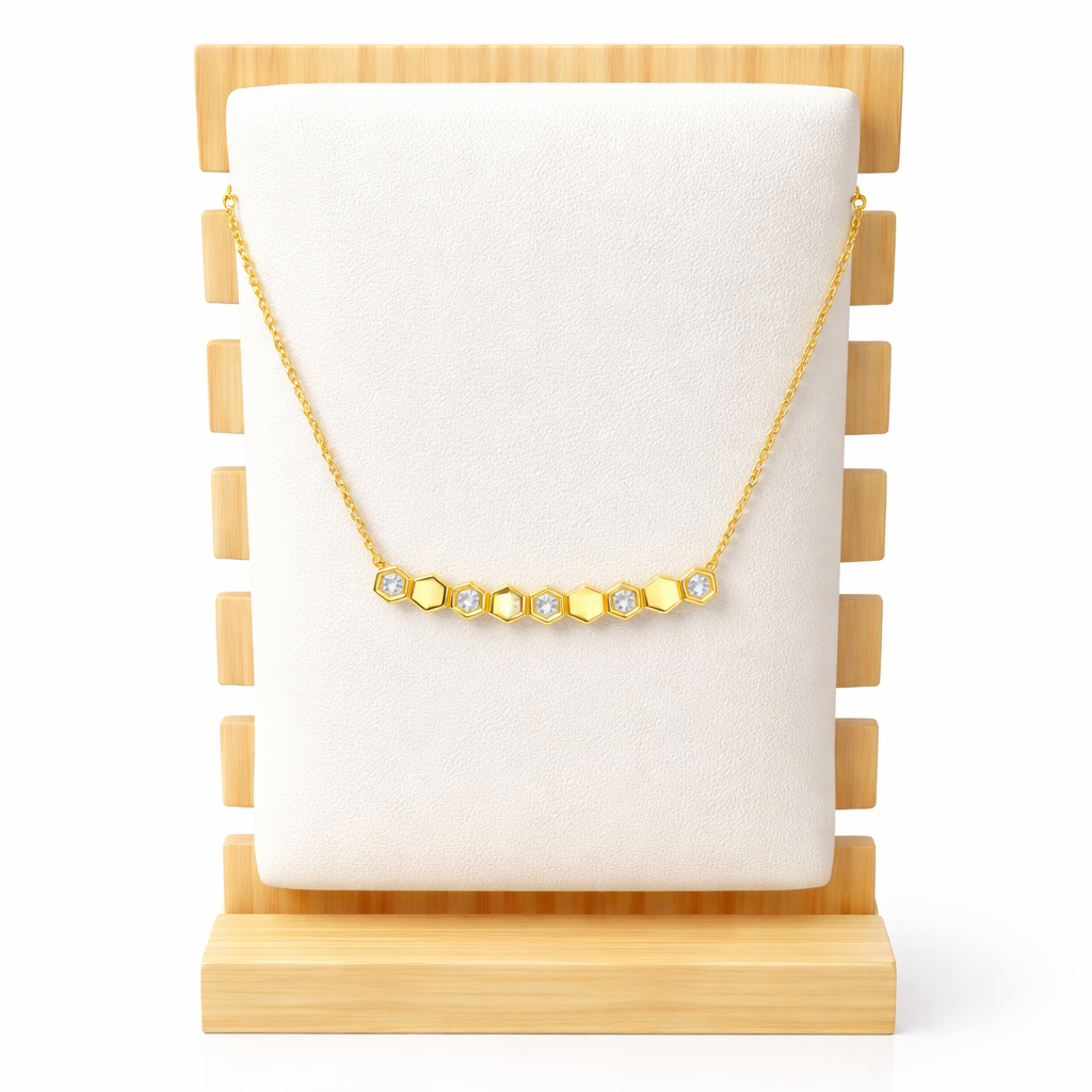 Gold necklace with hexagonal beads on a white cushion, displayed on a wooden stand.