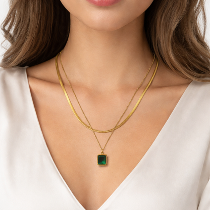 Gold necklace with a green pendant worn by a model in a white top