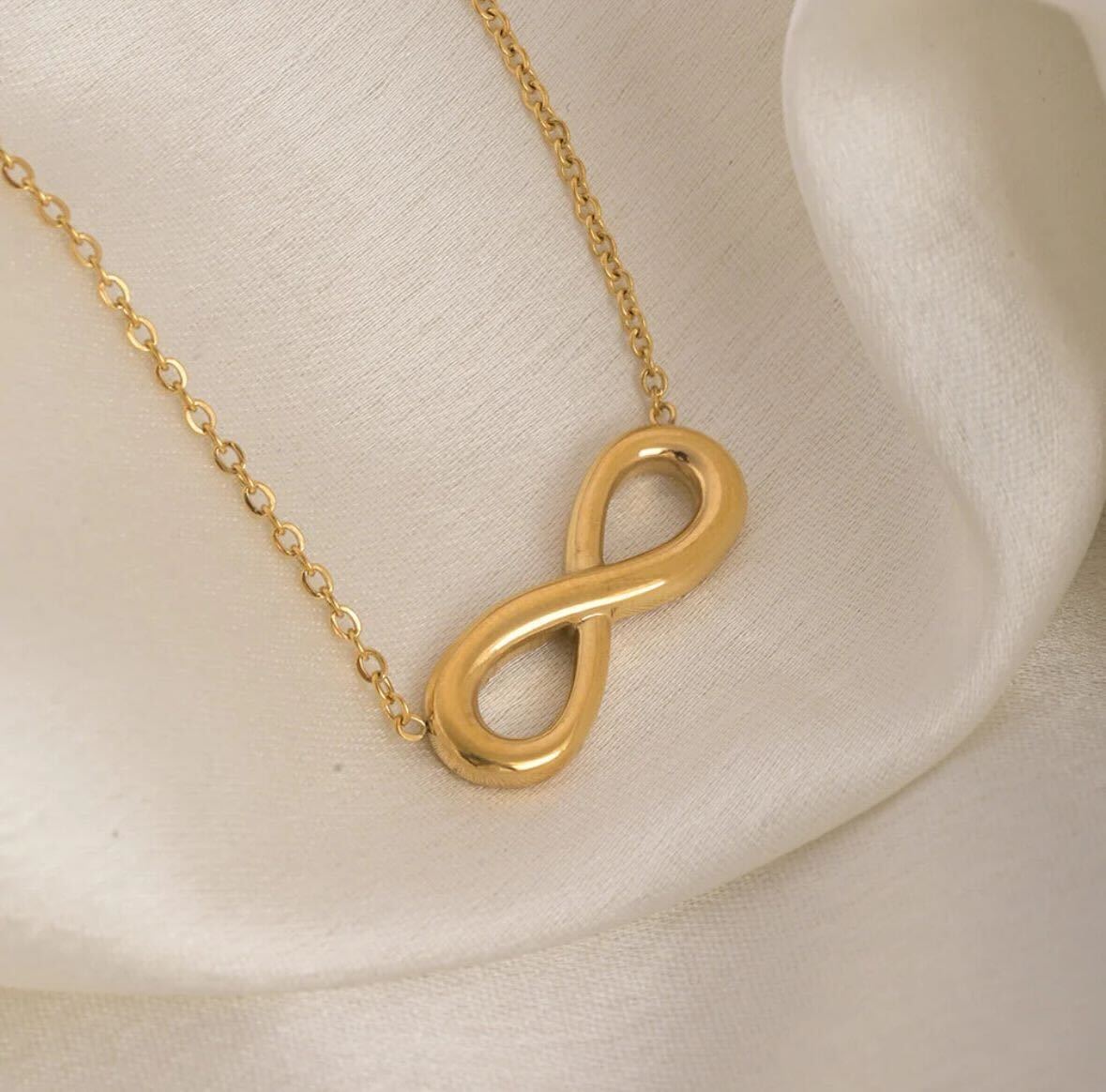Gold infinity necklace on a beige background