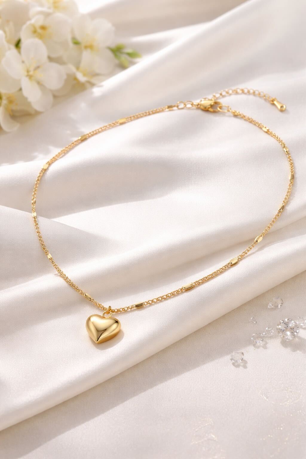 Gold heart-shaped pendant necklace on a soft white fabric background with flowers.