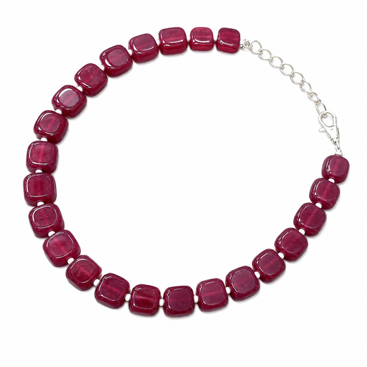 A beaded necklace featuring round, cushion-cut dark red gemstone beads connected by small silver-toned spacers, with a silver chain extender and lobster clasp, shown on a plain white background.