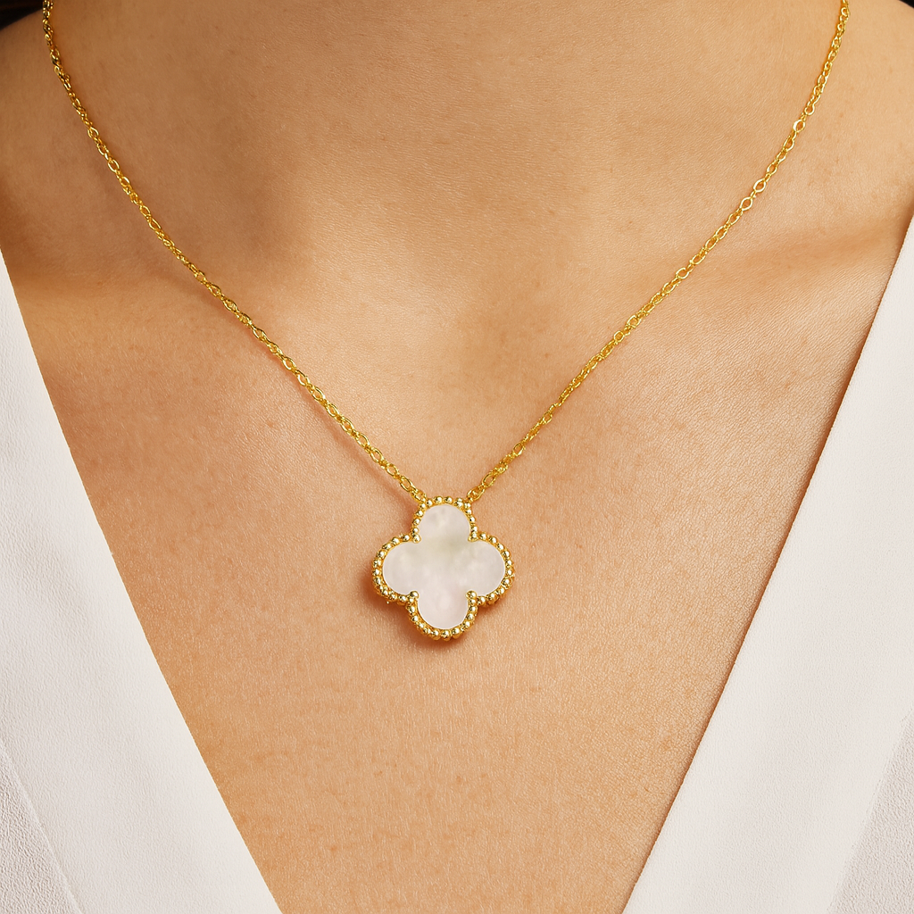 Gold necklace with a clover-shaped pendant on a person wearing a white top.

