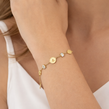 Gold bracelet with various charms on a wrist against a neutral background