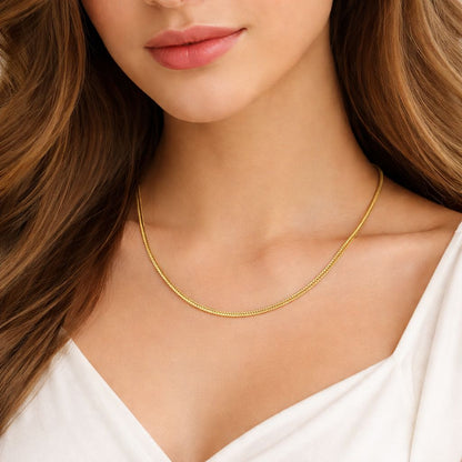 A close-up of a woman wearing a delicate gold chain necklace with a snake-style link design, paired with a white V-neck top.