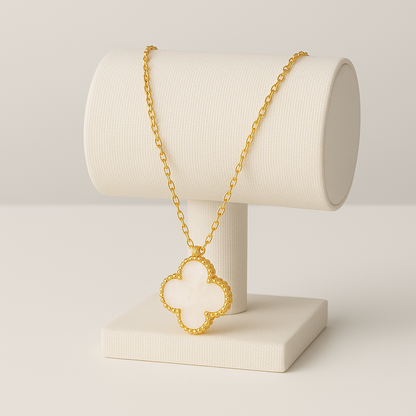 Gold necklace with a clover-shaped pendant on a white stand against a light gray background