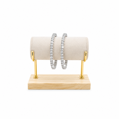 Two silver-toned tennis bangles with clear stones, displayed on a beige velvet jewelry roll mounted on a gold stand with a light wood base, against a white background.