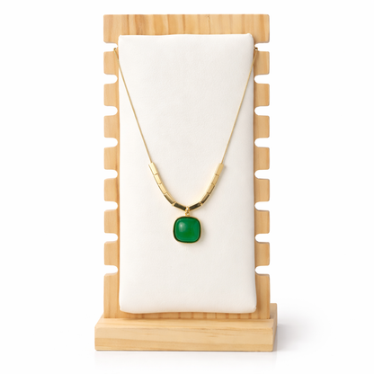 Gold necklace with a green pendant on a wooden stand with a white background