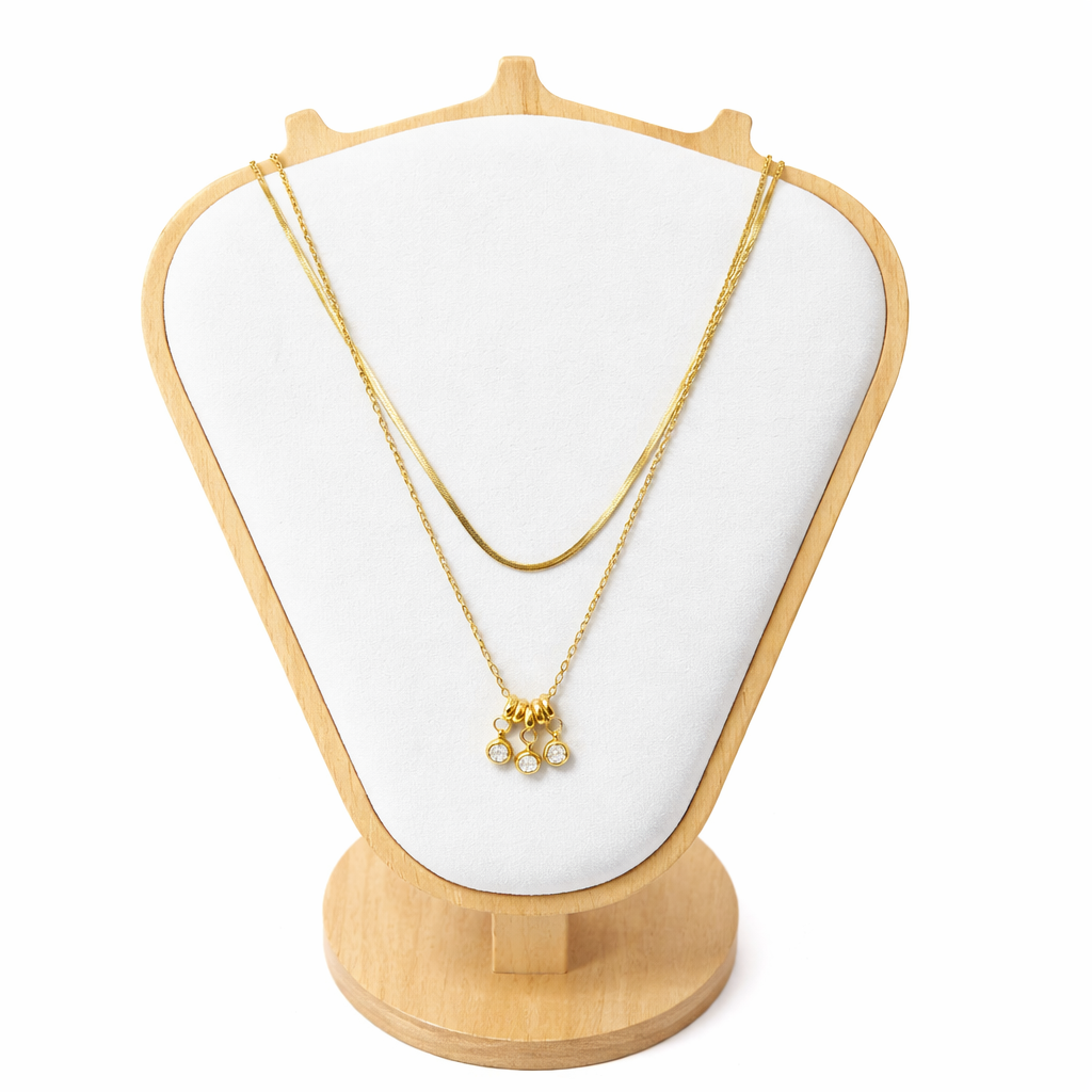 Gold necklace on a white cushioned jewelry stand with a wooden base