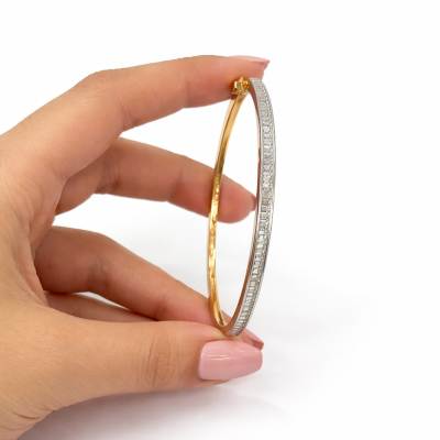 Gold and silver bangle held by a hand on a white background