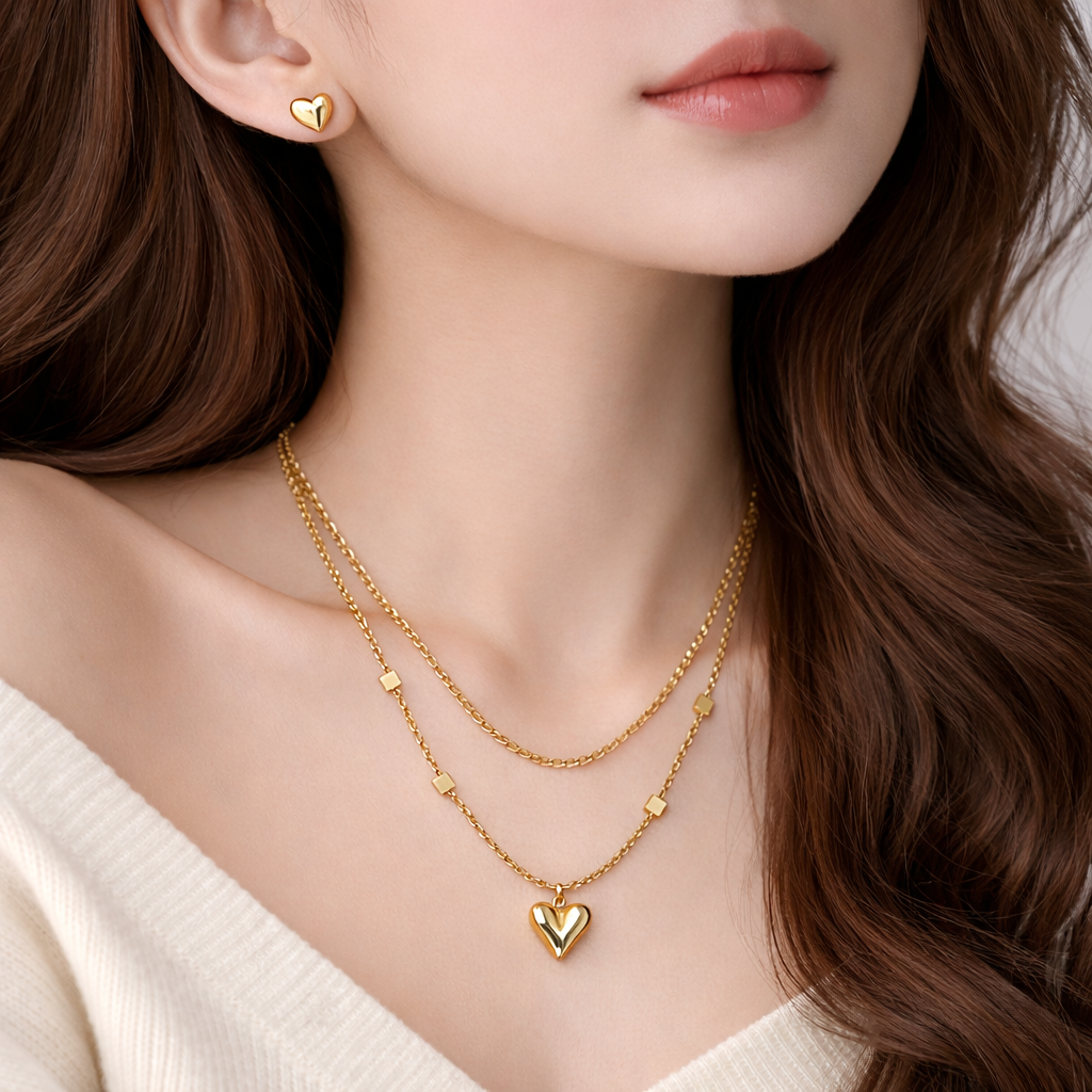Close-up of a person wearing a gold necklace with a heart pendant and matching earrings.