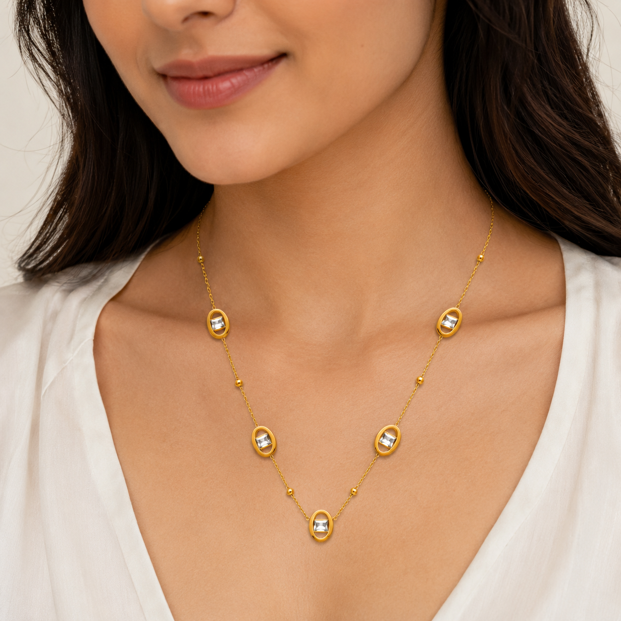 Gold necklace with clear stones worn by a model against a neutral background