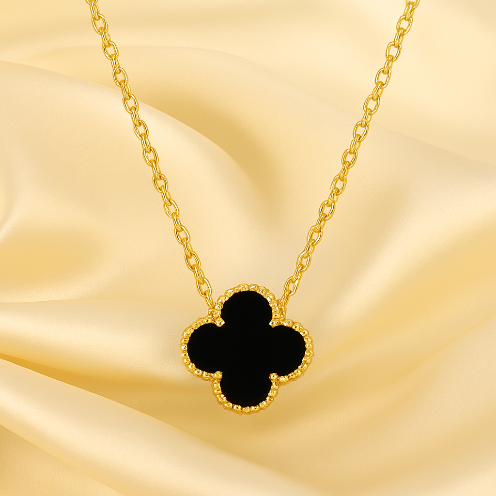 Gold necklace with a black clover pendant on a gold fabric background