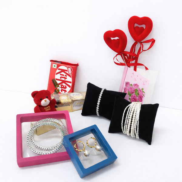 Jewelry set with pearl necklaces on black pillows, KitKat bar, teddy bear, and heart-shaped decorations on a white background.