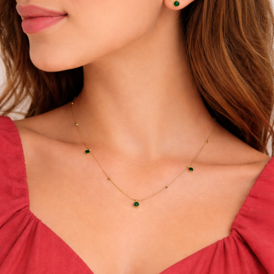 Close-up of a woman wearing a gold necklace with green gemstones and matching earrings.