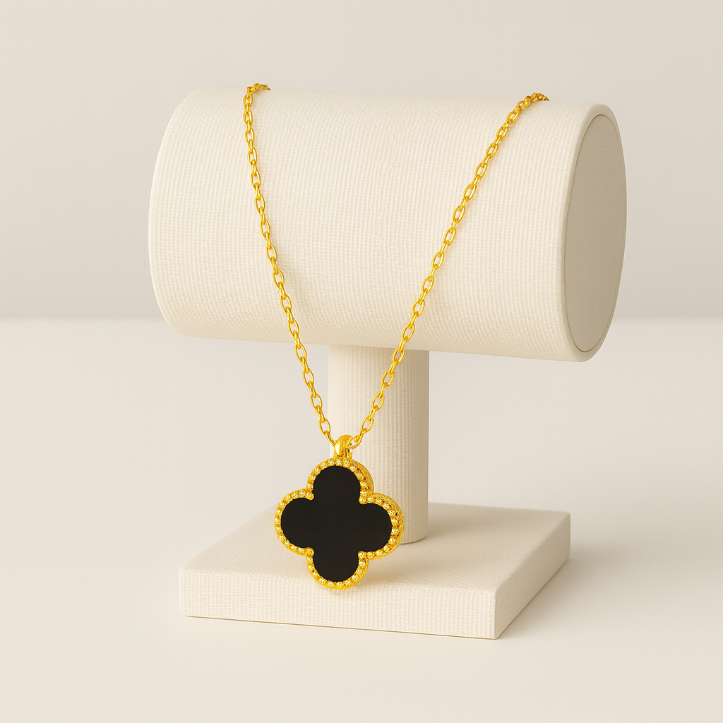 Gold necklace with a black clover pendant on a white stand against a beige background