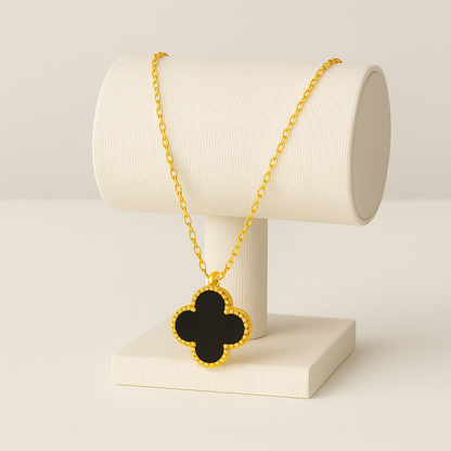 Gold necklace with a black clover pendant on a white stand against a beige background