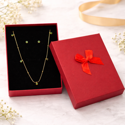 Gold necklace in an open red gift box with a red ribbon on a light background.