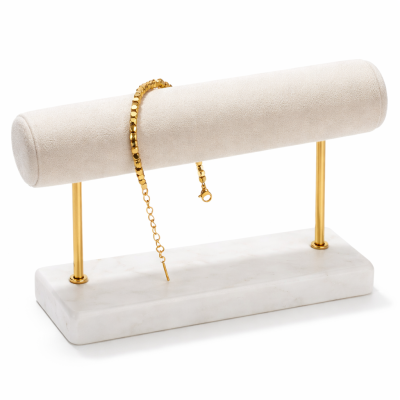 Gold bracelet on a white jewelry stand with a marble base