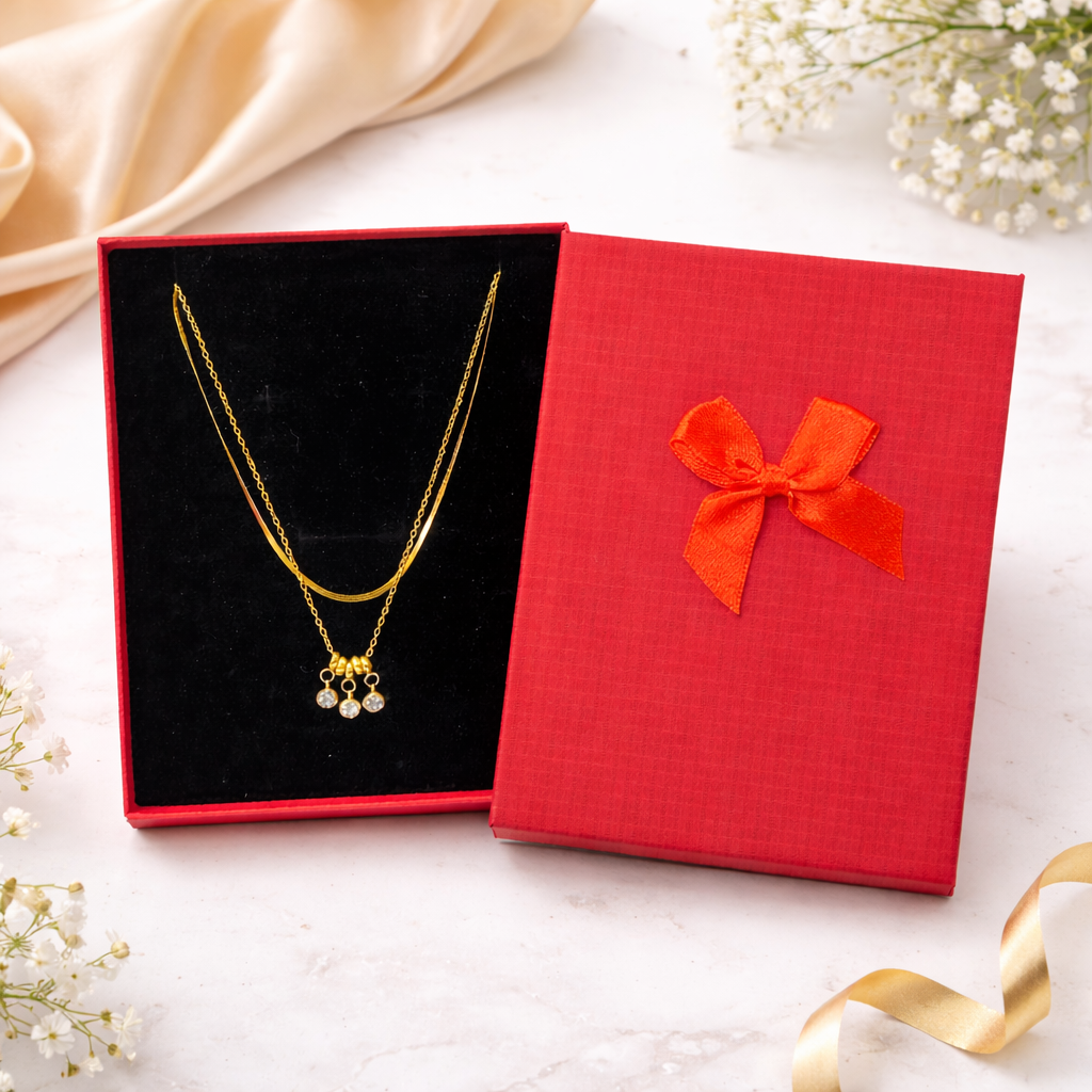 Gold necklace in a red gift box with a bow on a white surface with flowers.