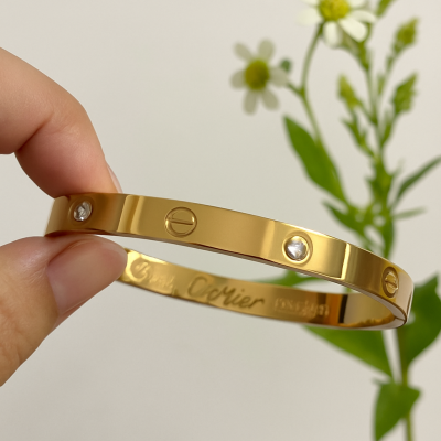 Gold bracelet held by a hand with a blurred natural background