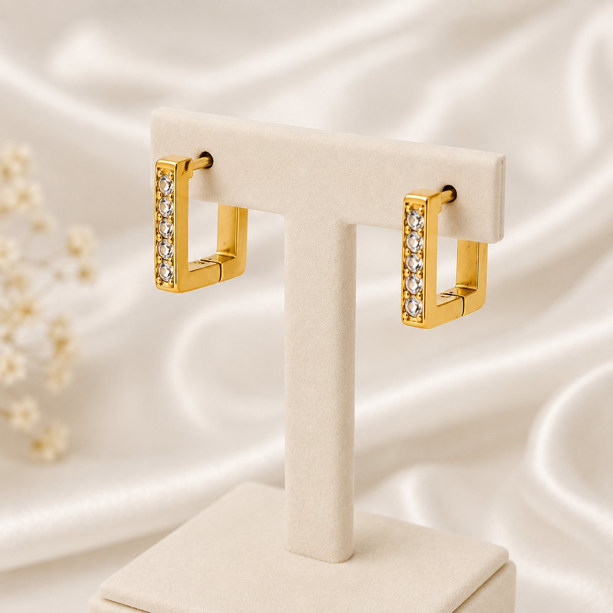 Gold hoop earrings with clear stones on a white stand against a soft, light background