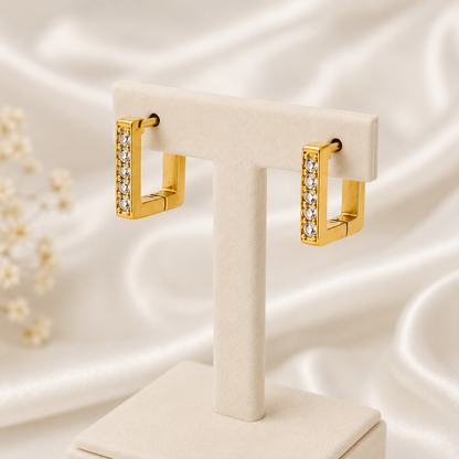 Gold hoop earrings with clear stones on a white stand against a soft, light background