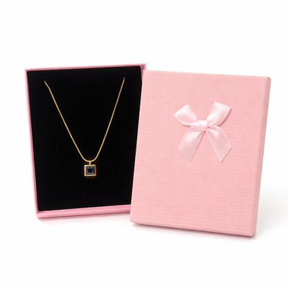 Necklace in a black box with a pink jewelry box featuring a bow on a white background