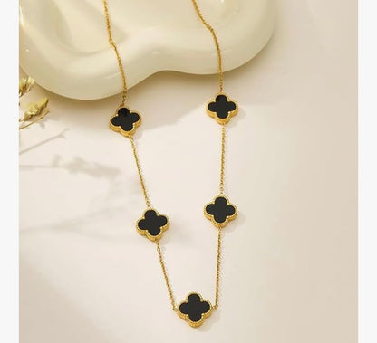 Gold necklace with black clover-shaped pendants on a beige background

