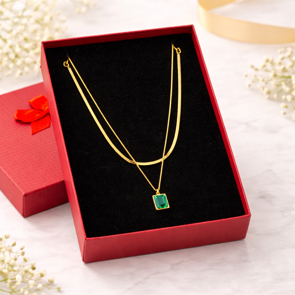Gold necklace with a green pendant in a red box on a light background