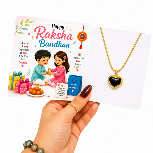 A hand holds a Raksha Bandhan gift card next to a gold heart pendant necklace on a white display card. The card features festive illustrations of a boy and girl tying a cord, wrapped gifts, orange sweets, and Hindi text celebrating Raksha Bandhan.