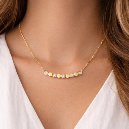 Gold necklace with hexagonal gemstones on a person wearing a white top