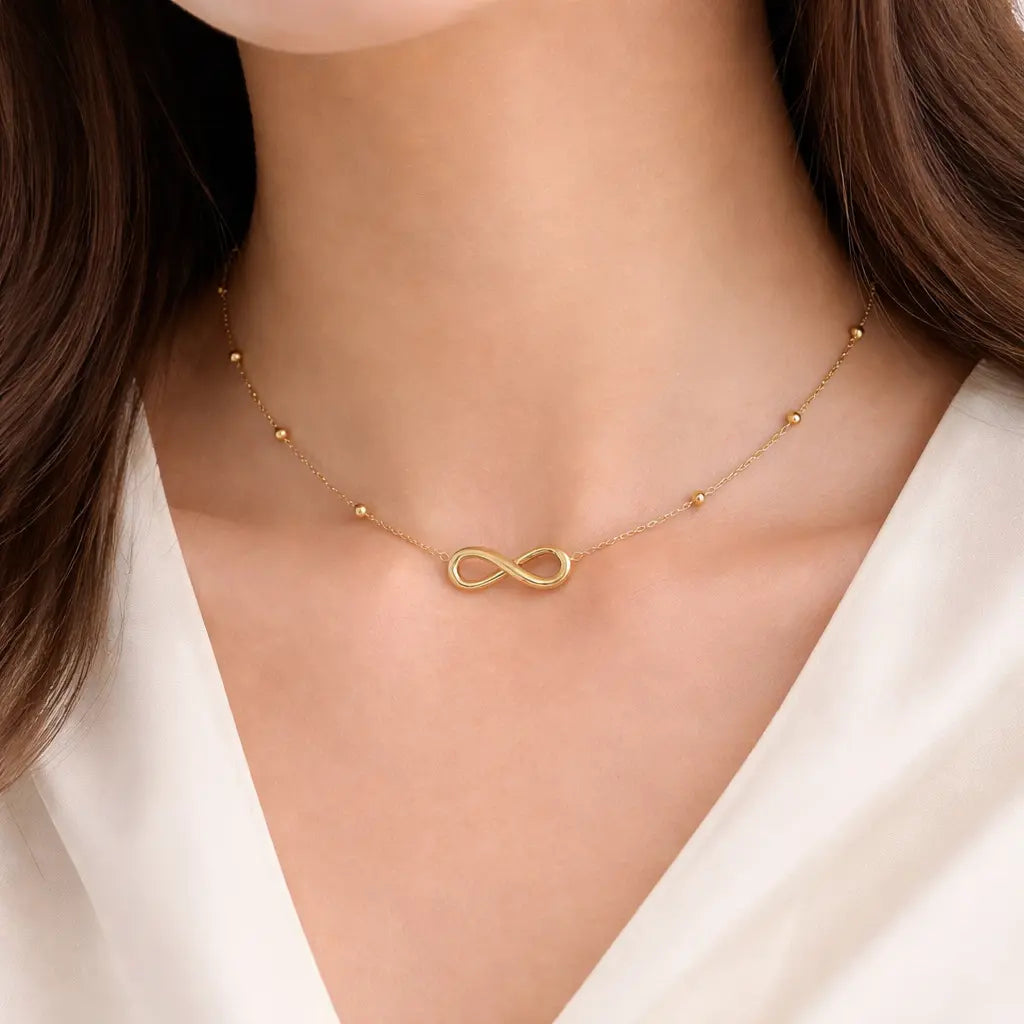 Gold infinity necklace on a person wearing a white top