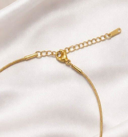 A gold-toned snake chain necklace with a lobster clasp and adjustable extension chain, displayed on a soft white satin fabric background.