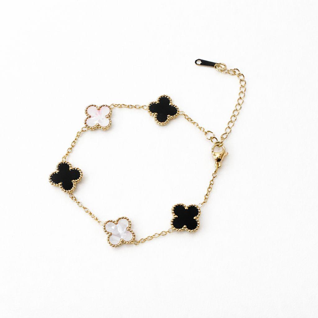 A gold-tone chain bracelet featuring five alternating black and white clover-shaped charms with gold beaded borders, displayed on a clean white background.