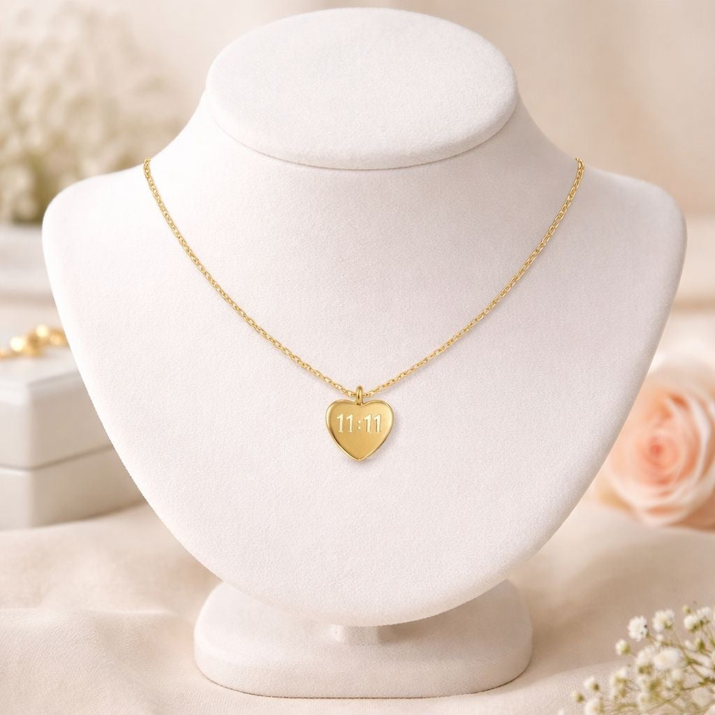 A gold heart pendant necklace engraved with '11.11' is displayed on a white jewelry bust.