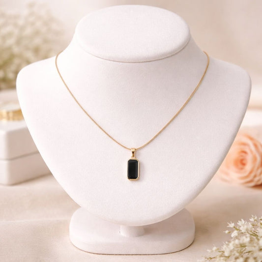 Gold necklace with a black pendant on a white mannequin bust with a soft, blurred background.