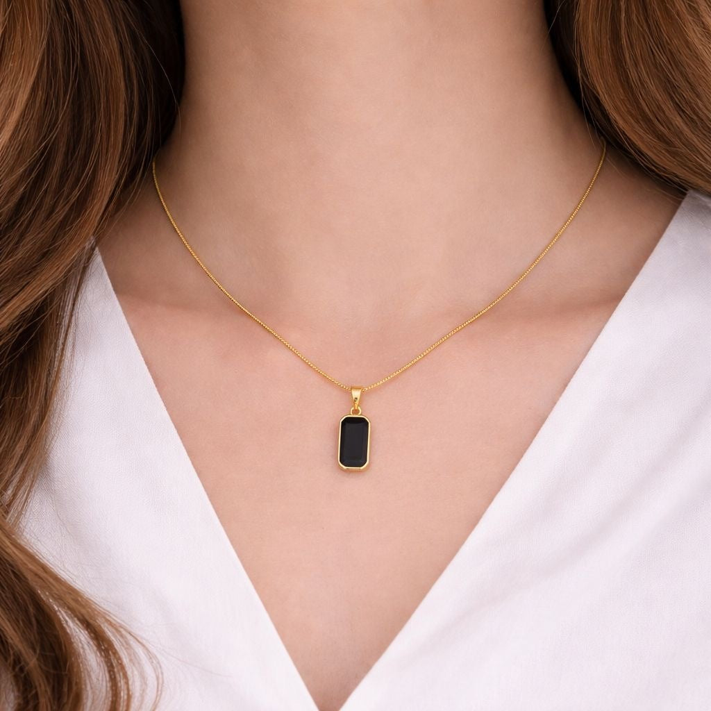 Gold necklace with a black pendant worn by a person in a white shirt.