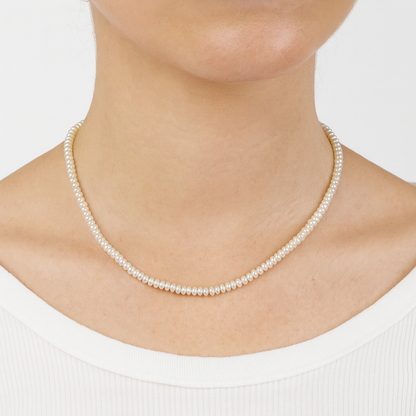 Pearl necklace worn by a person on a plain background

