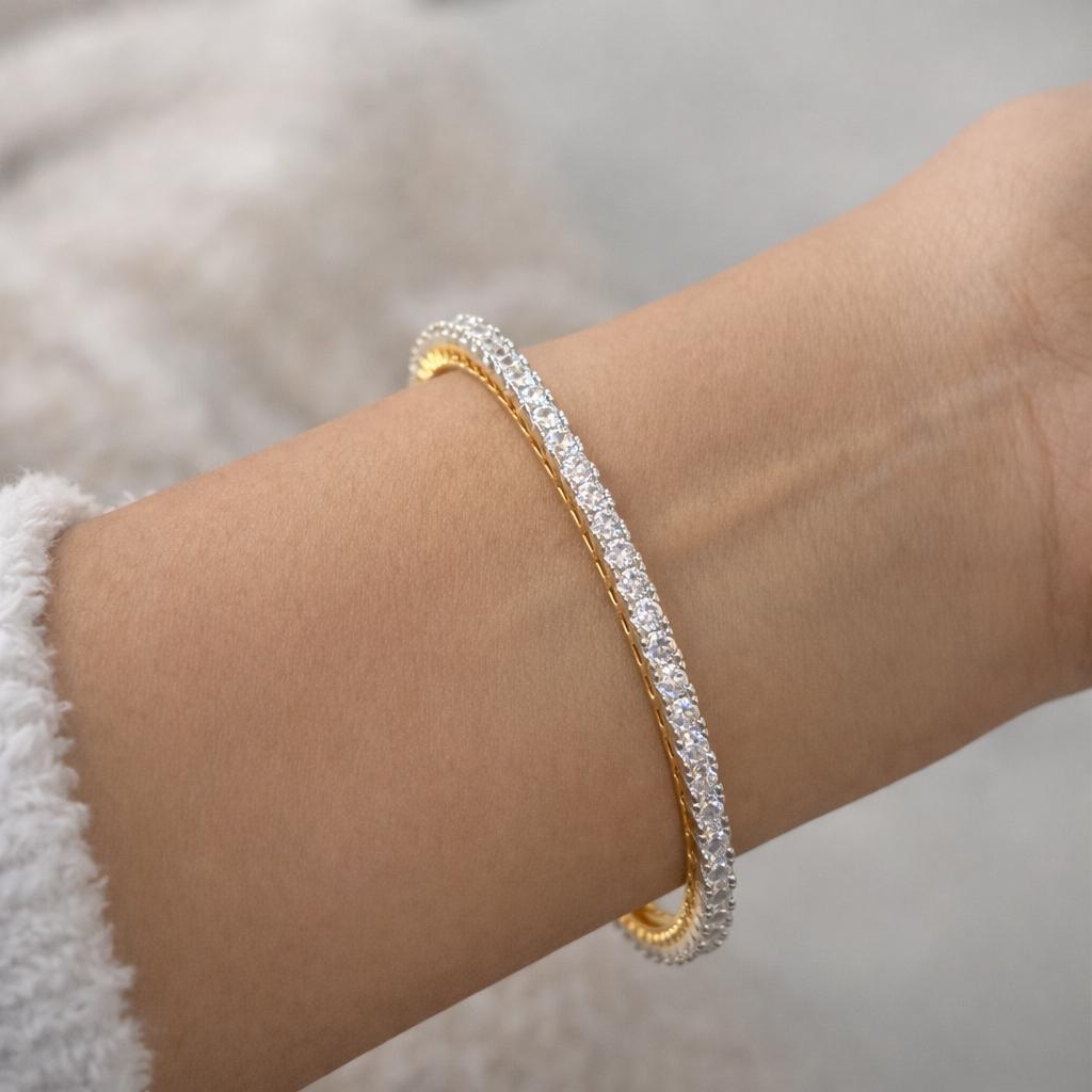 Gold bracelet with clear stones on a wrist against a neutral background