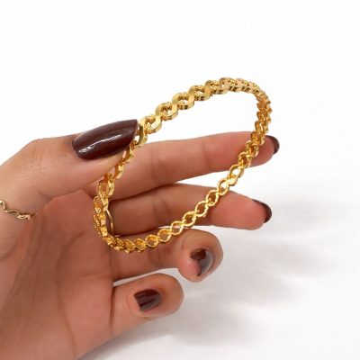 Gold chain bracelet held by a hand with dark nail polish on a white background