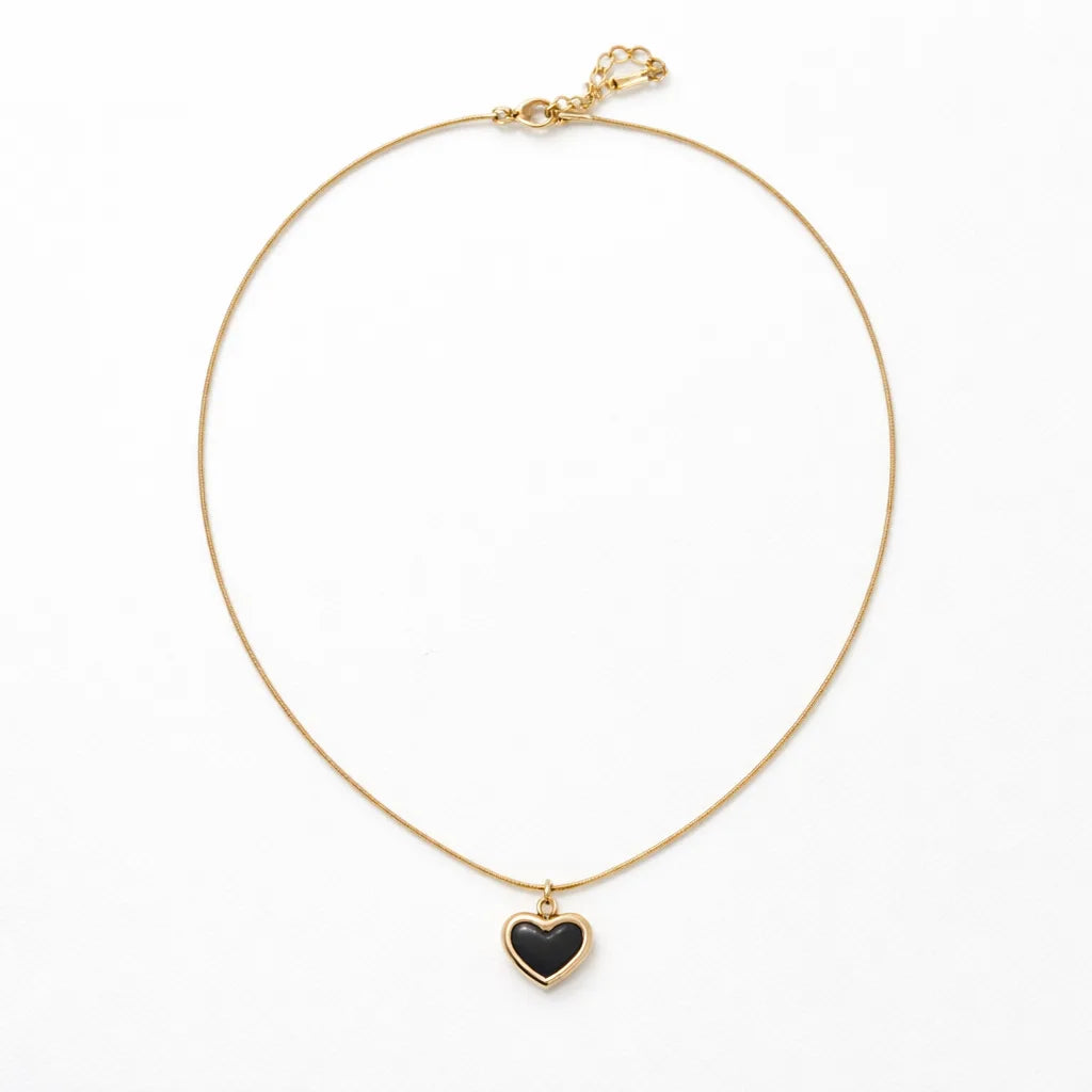 Gold necklace with a black heart pendant on a white background