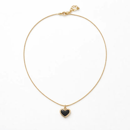 Gold necklace with a black heart pendant on a white background