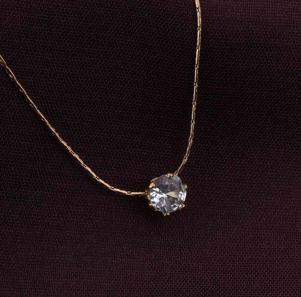 Gold necklace with a clear gemstone on a dark fabric background