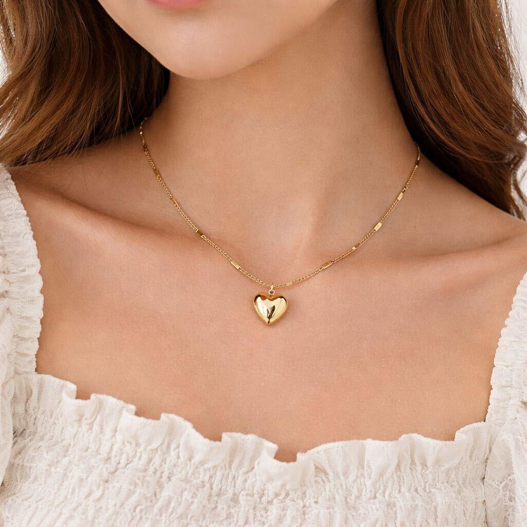 Gold necklace with a heart pendant worn by a person in a white top.